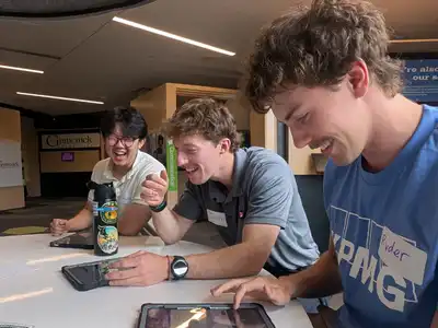 Three male students laugh while holding iPads